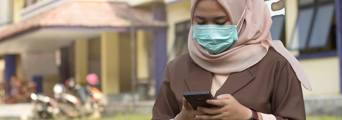 woman with pink scarf wearing mask looking at mobile phone